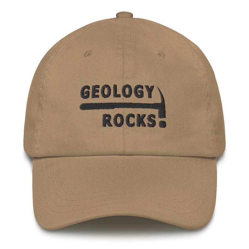 Puede incluir: Una gorra de b&eacute;isbol de color beige con bordado negro que dice "GEOLOGY ROCKS!" con un gr&aacute;fico de un pico.