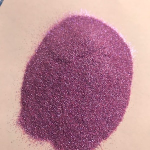 Puede incluir: Un montón de purpurina fina e iridiscente de color morado. La purpurina es muy fina y tiene un ligero brillo.