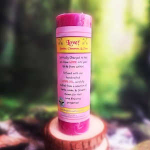 May include: Pink candle with a white label that reads "Love! Jasmine, Cinnamon, & Clove" and "Spiritually Charged to help you draw LOVE into your life & from within!" The candle is infused with handcrafted love oil, carefully crafted from a selection of herbs, roots, and flowers chosen for their love drawing properties.