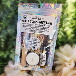 May include: A holographic pouch containing a Spirit Communication spell kit. The label lists contents including oil, a tealight, and a herb blend. Inside are a white tealight, a small glass vial of oil, a bag of dried herbs, and a silver feather charm.