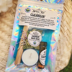 May include: A spell kit for cleansing with a tealight, a vial of oil, a bundle of herbs, and a charm. The kit is packaged in a clear plastic bag with a holographic iridescent finish. The label reads "SPELL KIT CLEANSIN'" and includes instructions for use.