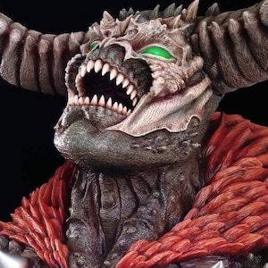 Puede incluir: Un busto esculpido detallado de un demonio con cuernos rojos, una capa roja y una expresión amenazante. El demonio tiene ojos verdes y dientes afilados. La escultura está hecha de un material gris oscuro y tiene una superficie texturizada.