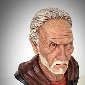 May include: A detailed bust sculpture of an elderly man with white hair and a white beard. The sculpture has a red shirt and a dark brown cloak. The base is black with a puzzle-piece design. The text "1/3 BUSTER STUDIO" is at the bottom.