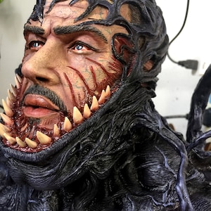 May include: A close-up of a black and red Venom bust. The bust is made of a detailed, textured material and features a menacing expression with sharp teeth.