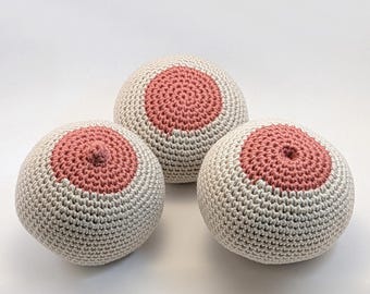 Op de afbeelding: Drie handgemaakte gehaakte bollen, elk met een lichtbeige basis en een cirkelvormig, roze gekleurd centrum. De bollen zijn gerangschikt op een wit oppervlak, waarbij de gedetailleerde textuur van het haakwerk wordt getoond. Het ontwerp is eenvoudig en artistiek.