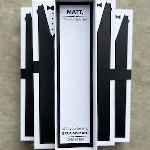 Puede incluir: Tres cajas blancas con dise&ntilde;os de esmoquin negros y el texto "MATT, Time to Suit Up!" y "Will you be my, GROOMSMAN? CHASTEN". Las cajas est&aacute;n atadas con cintas negras, perfectas para una boda.