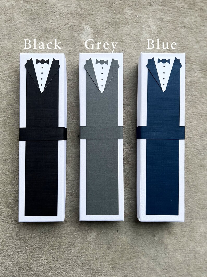 Puede incluir: Tres cajas de regalo rectangulares, cada una con un dise&ntilde;o de esmoquin. Las cajas son negras, grises y azules, con camisas blancas, pajaritas negras y una banda negra. El texto "Black", "Grey" y "Blue" est&aacute; encima de cada caja.