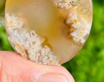 May include: A round, translucent agate stone with a white and yellow pattern. The stone is about 2 inches in diameter and has a smooth, polished surface.