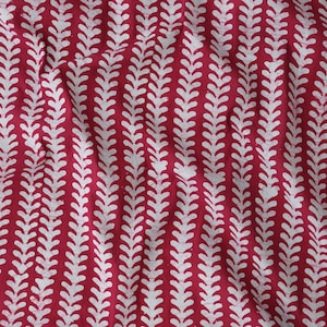 May include: Red fabric with a white repeating pattern of stylised leaves. The leaves are arranged in vertical rows.