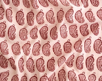 May include: A pink fabric with a repeating pattern of red paisley shapes. The paisley shapes are outlined in white and have a white swirl design inside.