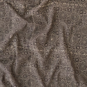 Puede incluir: Una tela negra con un patrón crema de diseños circulares repetidos. La tela está arrugada y tiene una superficie texturizada.