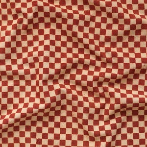 Könnte beinhalten: Ein Stoff mit einem sich wiederholenden Muster aus roten und cremefarbenen Quadraten. Die Quadrate sind in einem Schachbrettmuster angeordnet und erzeugen eine optisch ansprechende und strukturierte Oberfläche. Der Stoff scheint leicht zerknittert zu sein, was seine taktile Qualität erhöht.