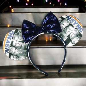 Puede incluir: Orejas de Minnie Mouse de lentejuelas azules con un logotipo *NSYNC* blanco y azul y una foto de los miembros de la banda en las orejas.