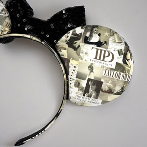 May include: Black and white mouse ears headband with a black sequin bow. The ears are covered in a collage of images and text, including the words "Taylor Swift" and "The Tortured Arts Department".