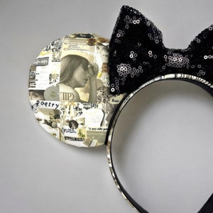 May include: Black and white patterned fabric mouse ears with a black sequin bow. The fabric features a collage of text and images.