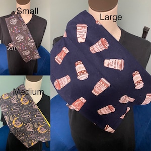 Puede incluir: Tres protectores de cuello de diferentes tamaños, cada uno con un patrón único. El pequeño tiene un diseño floral, el mediano presenta serpientes y lunas, y el grande muestra tazas de café con texto.