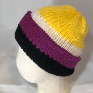 May include: A yellow, white, purple and black striped knitted beanie hat.