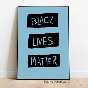 Op de afbeelding: Een lichtblauwe poster met de woorden "BLACK LIVES MATTER" in zwart, handgeschreven tekst op een witte achtergrond. De woorden staan in drie aparte rechthoekige vakken.