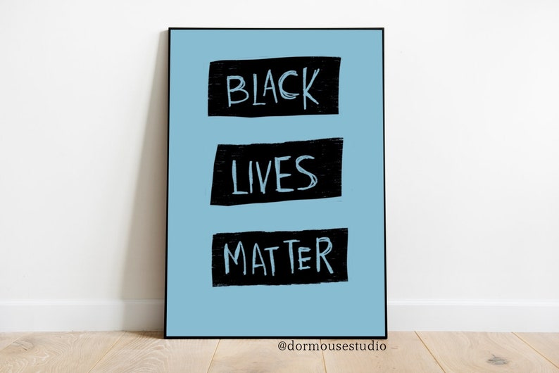 Op de afbeelding: Een lichtblauwe poster met de woorden "BLACK LIVES MATTER" in zwart, handgeschreven tekst op een witte achtergrond. De woorden staan in drie aparte rechthoekige vakken.