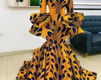 May include: A long-sleeved, off-the-shoulder dress with a fitted bodice and a flowing skirt. The dress is made of a yellow and blue fabric with a peacock feather pattern. The dress has large, ruffled sleeves.