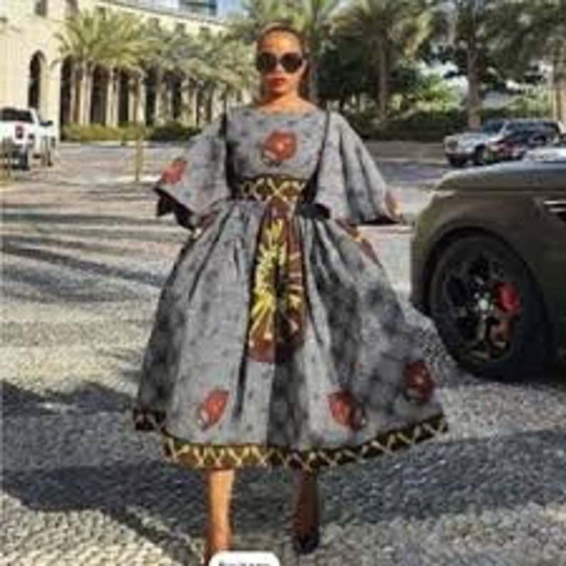 May include: A gray and brown patterned dress with a fitted bodice and a full skirt. The dress has a round neckline and 3/4 sleeves. The dress is cinched at the waist with a brown belt.