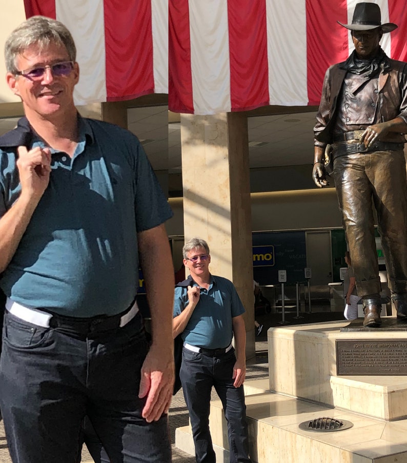 Man shown in white buckleless belt beside John Wayne statue in Orange County SNA airport.  Belt can be worn through airport security.