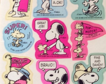 May include: A sheet of colorful stickers featuring the cartoon character Snoopy. The stickers have various phrases such as "First Rate", "Super", "Great Job", "A.O.K.", "Terrific", "Top Notch", "Smart U", "Bravo", and "Fine and Dandy".