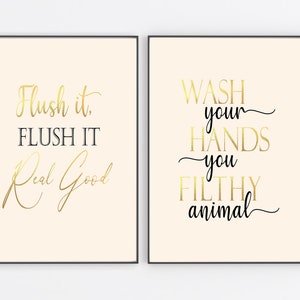 Puede incluir: Dos impresiones enmarcadas con letras doradas sobre un fondo crema. La primera impresi&oacute;n dice "Flush it. FLUSH IT Real Good". La segunda impresi&oacute;n dice "WASH your HANDS you FILTHY animal".
