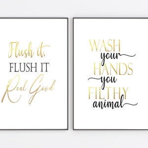 Puede incluir: Dos impresiones enmarcadas blancas con texto negro y letras doradas. La primera impresi&oacute;n dice "Flush it. FLUSH IT Real Good". La segunda impresi&oacute;n dice "WASH your HANDS you FILTHY animal".