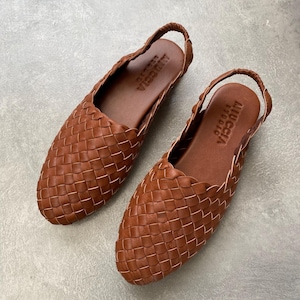 Può includere: Un paio di sandali in pelle intrecciata marrone con cinturino slingback. I sandali hanno il nome del marchio "A.P.C." in rilievo sul sottopiede.