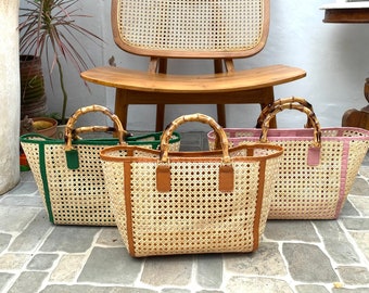 May include: Three woven rattan tote bags with leather handles. The bags are in green, brown, and pink. The bags are sitting on a tiled floor in front of a wooden chair.