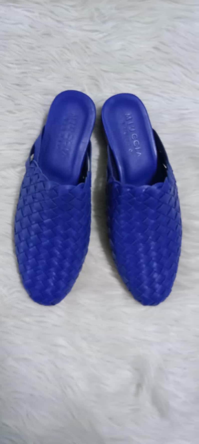Puede incluir: Un par de mules de cuero tejido azul con el nombre de la marca "MIU MIU" estampado en la plantilla.