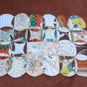 Può includere: Una trapunta patchwork fatta a mano con una varietà di tessuti fantasia in un mix di colori tra cui bianco, arancione, marrone, verde e giallo. La trapunta è composta da forme arrotondate collegate.
