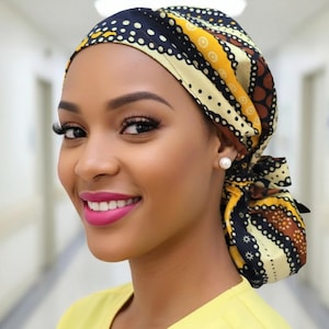 May include: A patterned head covering in shades of navy, yellow, and brown. The head covering is tied at the back. The person is wearing a yellow top and a pearl earring. The person is smiling.