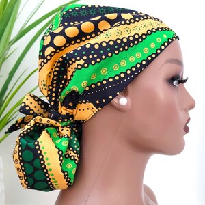 May include: A colorful head wrap featuring a vibrant pattern of yellow, green, and black circles and lines. The wrap is tied in a bow at the back, showcasing the intricate design. The head covering is designed to be worn on the head.