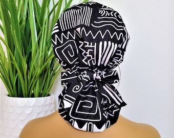 Puede incluir: Un gorro quirúrgico de patrón geométrico en blanco y negro. El gorro está atado en la parte posterior de la cabeza con un lazo.