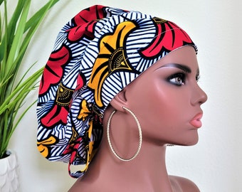 Puede incluir: Un gorro de quirófano blanco, azul, rojo y amarillo con estampado y un lazo en la parte posterior. El gorro se lleva en un maniquí con grandes pendientes de aro dorados.