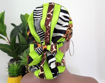Puede incluir: Un gorro quirúrgico verde, negro, blanco y marrón con estampado y un lazo en la parte posterior. El gorro está hecho de tela y tiene un estampado de cebra, jirafa y leopardo.