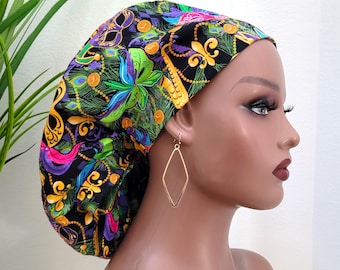 Puede incluir: Un gorro de quirófano negro con un estampado colorido de Mardi Gras con máscaras, cuentas y flores de lis. El estampado está sobre un fondo negro con detalles en verde, morado, dorado y rosa.