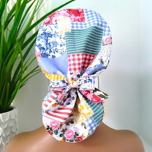 May include: A colorful patchwork scrub hat with a bow tie. The hat is made of various fabrics with floral, plaid, and striped patterns in shades of blue, red, green, yellow, and white.