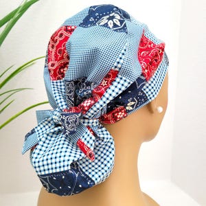 May include: A patchwork scrub cap featuring a mix of patterns and colors. The cap combines blue gingham, paisley, and floral prints in red and navy. A matching bow adds a decorative touch to this practical accessory.