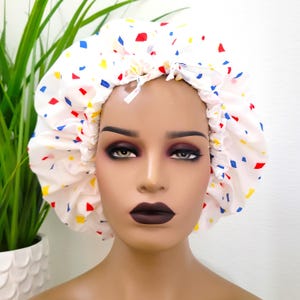 May include: White satin shower cap with a colorful confetti pattern in red, yellow, and blue.