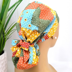 May include: A colorful patchwork scrub cap featuring a variety of patterns, including sunflowers, polka dots, and gingham. The cap is tied in a bow at the back and is made of various fabrics in shades of orange, green, yellow, and blue.