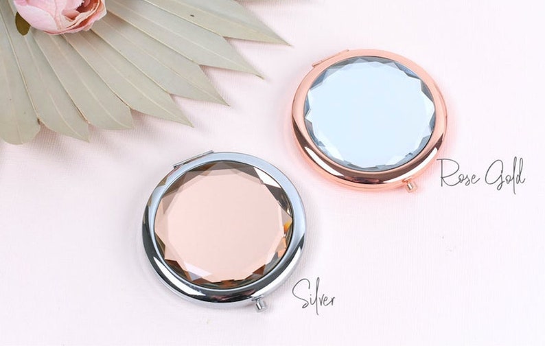 May include: Two compact mirrors with a faceted design. One mirror has a silver frame and a pink glass, the other has a rose gold frame and a clear glass. The text "Rose Gold" is written below the rose gold mirror and "Silver" is written below the silver mirror.