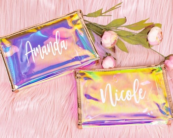 May include: Two iridescent clear makeup bags with gold zipper pulls. The bags have the names "Amanda" and "Nicole" printed in white on the front.