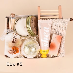 May include: A gift box containing a candle in a jar, a tube of shea lotion, a bath bomb, a bar of soap, a small bottle of matches, and a decorative sachet. The box is labeled "Box #5".