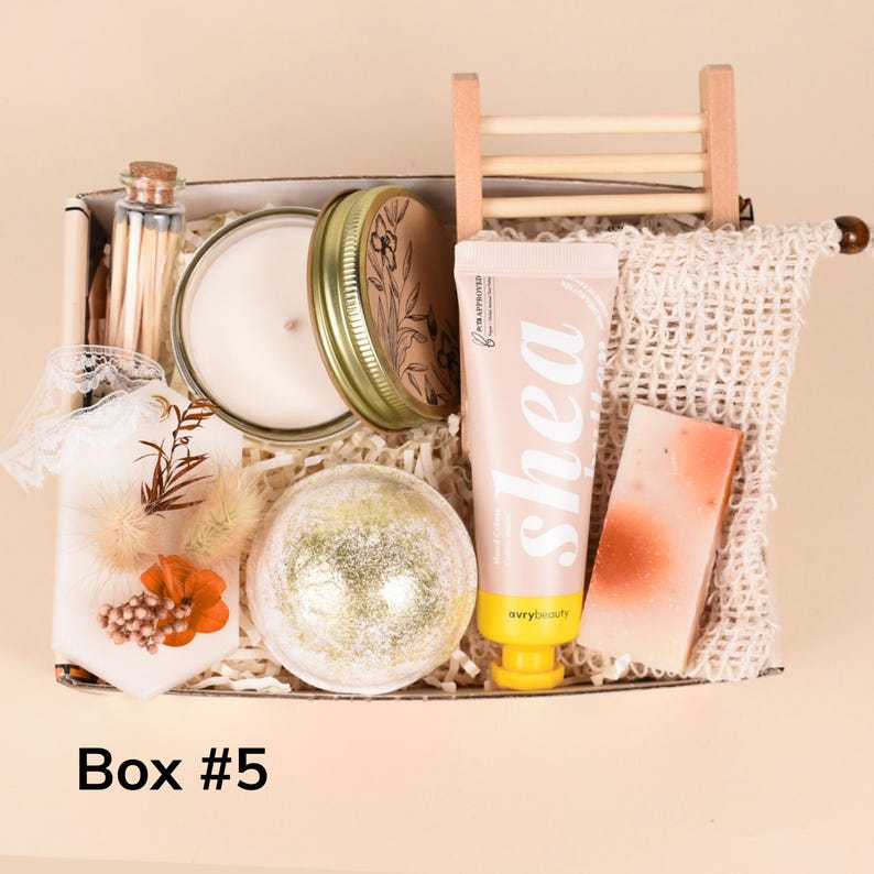 May include: A gift box containing a candle in a jar, a tube of shea lotion, a bath bomb, a bar of soap, a small bottle of matches, and a decorative sachet. The box is labeled "Box #5".