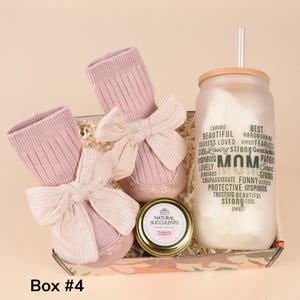 May include: A gift box containing pink baby shoes with bows, pink socks, a glass tumbler with the word "MOM" and related words, and a small jar. The tumbler has a bamboo lid and straw. The box is labeled "Box #4".