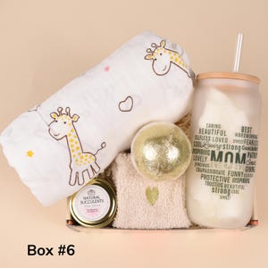 May include: A gift box containing a white giraffe-themed baby blanket, a gold bath bomb, a candle, a glass with the word "MOM" and related words, and a washcloth. The box is labeled "Box #6".