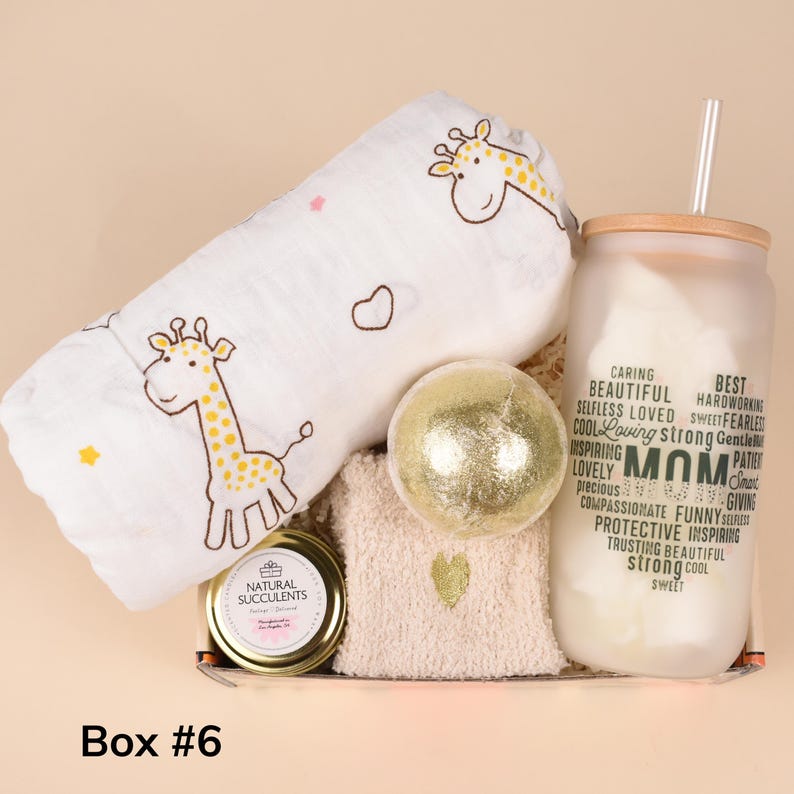 May include: A gift box containing a white giraffe-themed baby blanket, a gold bath bomb, a candle, a glass with the word "MOM" and related words, and a washcloth. The box is labeled "Box #6".